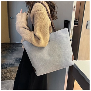 Detail of the large grey tote bag showing texture and brown leather strap on model shoulder