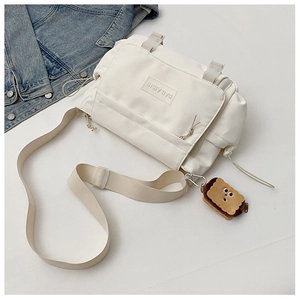 Détail du sac messager en nylon beige avec rabat et pendentif peluche biscuit mignon