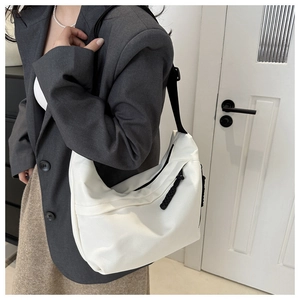 Close-up of white crescent crossbody bag styled with casual grey blazer and brown skirt
