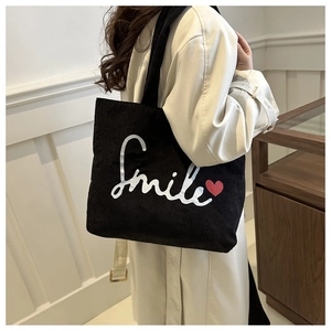 Close-up of black corduroy tote bag with embroidered Smile text and red heart detail