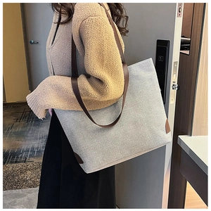 Detailed side view of the grey canvas tote bag with brown leather handles and reinforced corners