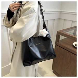 Close-up of black glossy leather tote bag with fashion label and white plush star charm
