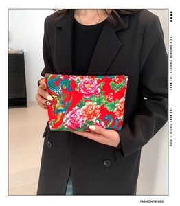 Close-up of woman holding red floral clutch bag with phoenix and peony pattern