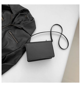 Flat lay of a minimalist black leather square crossbody bag with a slim strap and matte finish