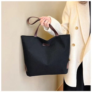 Detail of black canvas tote bag with brown leather handles and fashion label detail