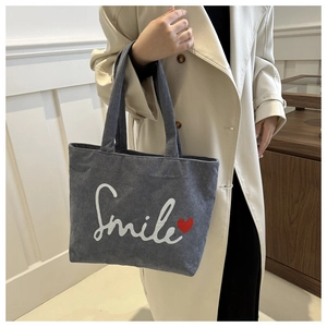 Detailed texture of grey corduroy tote bag featuring Smile text and red heart embroidery