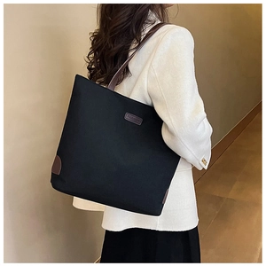 Detail of black canvas tote bag with fashion leather patch and slim brown straps
