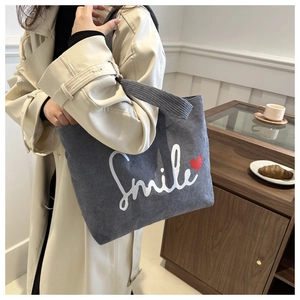 Close-up of gray corduroy tote bag with Smile print and red heart detail on a model