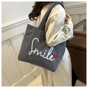 Detail view of large grey corduroy tote bag with Smile print worn by a fashion model