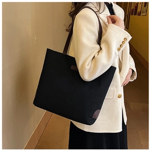 Detail of the black tote bag with brown leather straps and fashion label in a home setting