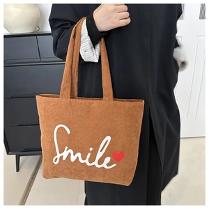 Detail of brown corduroy tote bag featuring Smile text and red heart embroidery