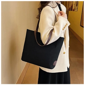 Detail of black canvas tote with brown leather trim carried on shoulder for daily commute