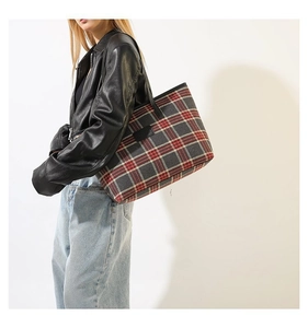 Detail of red and grey tartan tote bag with black leather straps on a model