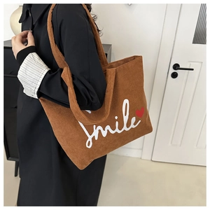 Close-up of brown corduroy tote bag showing the Smile text and red heart embroidery detail