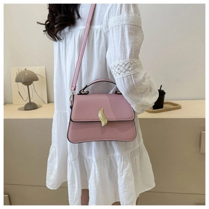 Sac à bandoulière rose mat porté avec une robe en dentelle blanche dans un décor doux