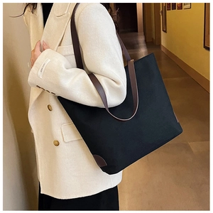 Detail of black canvas tote bag with brown leather straps and base patches on model shoulder