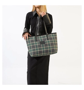Close-up of green plaid tote bag with black leather straps and detailed logo patch