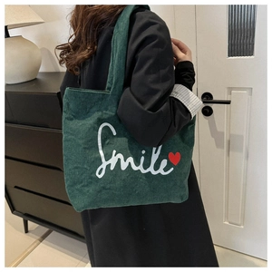 Close-up of deep green corduroy tote bag featuring white Smile text and red heart
