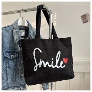 Detail of black corduroy tote bag with Smile print hanging on a metal hanger