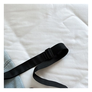 Dettaglio della tracolla regolabile in nylon nero su borsa in denim blu chiaro