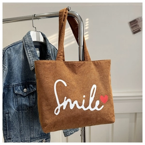 Detail of a brown corduroy tote bag featuring a white Smile text and red heart print