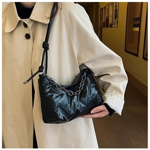 Détail du sac sous le bras noir matelassé avec chaîne argentée et bandoulière nouée