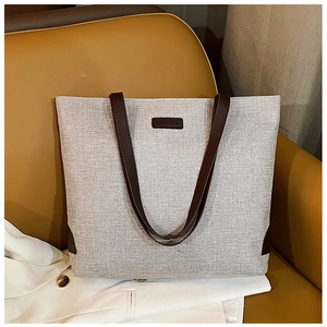 Detail of canvas tote bag showing fashion leather patch and contrast handle straps