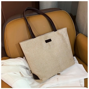 Detail of canvas tote bag with brown leather straps and fashion label on a sofa
