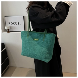 Gros plan d'un sac cabas vert en peluche avec écusson mode porté par un mannequin