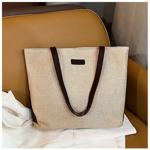 Close-up of beige woven tote bag with dark brown leather straps and fashion label detail
