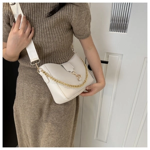 Detalle de bolso bandolera beige con cadena dorada y correa ancha de tela sobre modelo