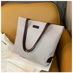 Detail of grey woven tote bag with brown leather handles and fashion logo on sofa