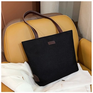 Close-up of black canvas tote bag with brown leather handles and fashion logo patch