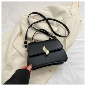 Détail du sac bandoulière en cuir noir avec fermoir feuille dorée sur un blazer blanc