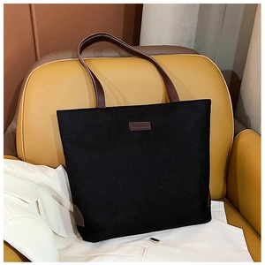 Detailed macro view of black canvas tote bag with brown leather straps and fashion label