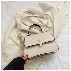 Détail du sac à main blanc crème avec fermoir doré posé sur un blazer beige de bureau