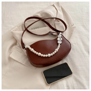 Détail d'un sac sous le bras demi-lune marron avec chaîne en perles et décor de cœur