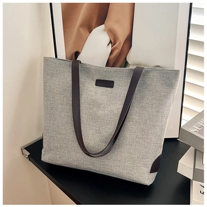 Detail of grey canvas tote bag featuring brown faux leather handles and fashion logo patch