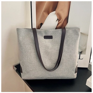 Close-up of a light grey tote bag with leather handles and fashion brand label detail