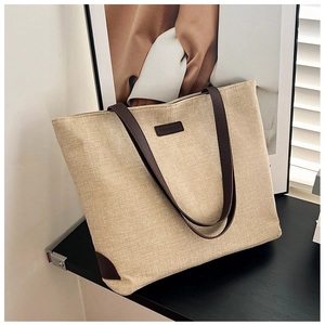 Close-up of a canvas tote bag with brown leather handles and fashion logo on a sleek surface