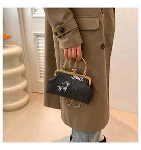 Detail view of a vintage-style black printed frame bag with a white deer motif and gold chain