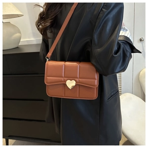 Borsa a tracolla trapuntata marrone con chiusura a cuore indossata da modella in casa