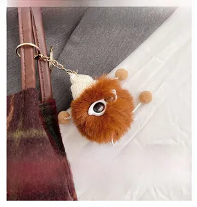 Close-up of a brown fuzzy monster charm with a white knit hat on a dark tote bag strap