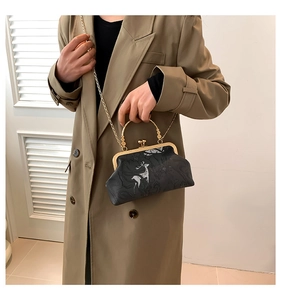 Detail of vintage black floral print crossbody bag with gold handle on khaki coat