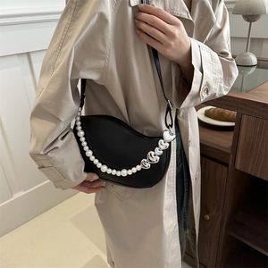Sac à bandoulière noir en demi-lune avec chaîne de perles et breloques cœur porté avec manteau