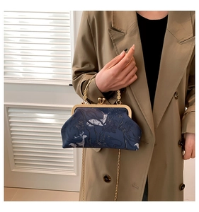 Close-up of deep blue kiss-lock bag with elk print, gold chain, and metal frame detail