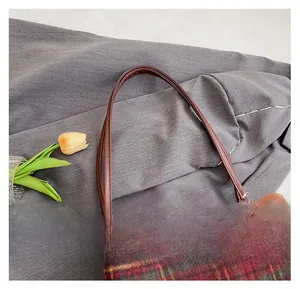 Detail of checkered wool tote bag showing brown leather strap and owl pendant charm