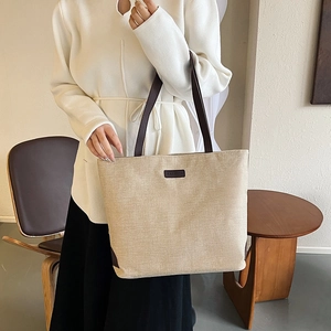 Minimalist beige linen tote bag with brown leather straps shown in a warm lifestyle setting