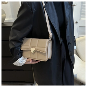 Dettaglio borsa a tracolla beige trapuntata con chiusura a cuore dorato su sfondo