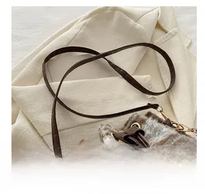 Détail de la bandoulière en cuir marron et de la texture en laine à carreaux du sac seau